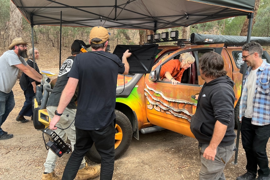 A film crew shoots a scene as an actor gets out of a car