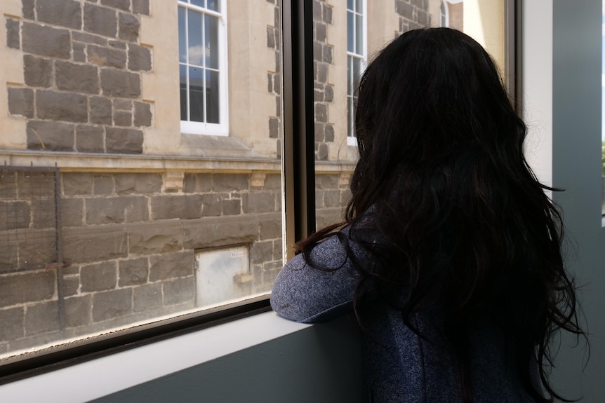 The back of a woman with dark hair looking out a window. 