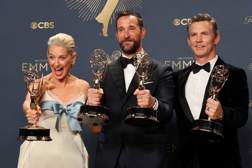 A woman and two men pose with Emmy awards