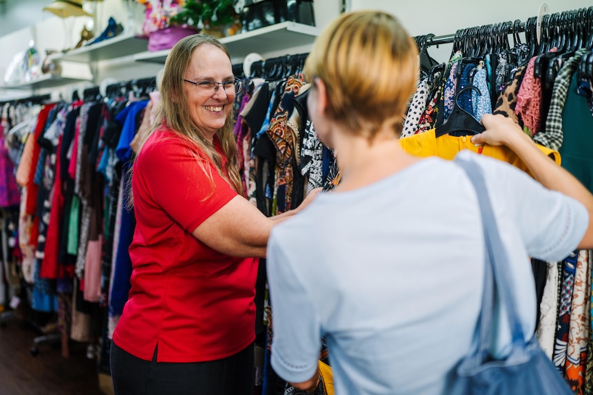 A volunteer smiles at another holding up an item of clothing.