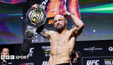 Alexander Volkanovski raises his featherweight title at the UFC 325 news conference