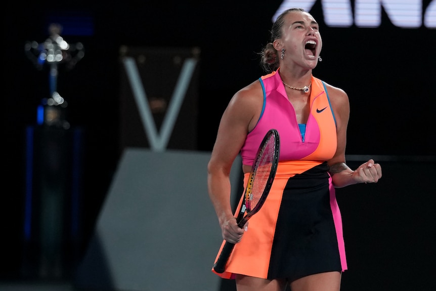 Aryna Sabalenka shouts and clenches her fist alongside the Daphne Akhurst Memorial Cup in the Australian Open final.