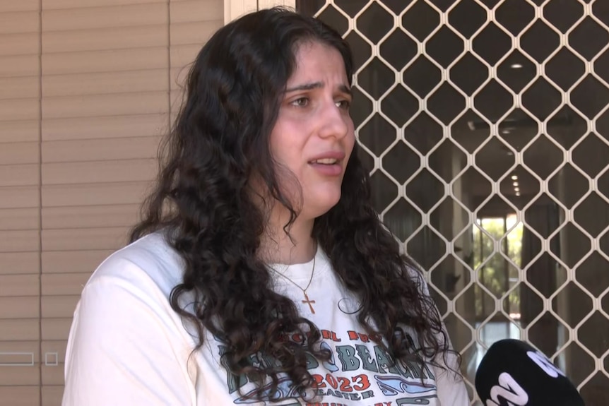 A woman with black hair stands outside a house looking worries 