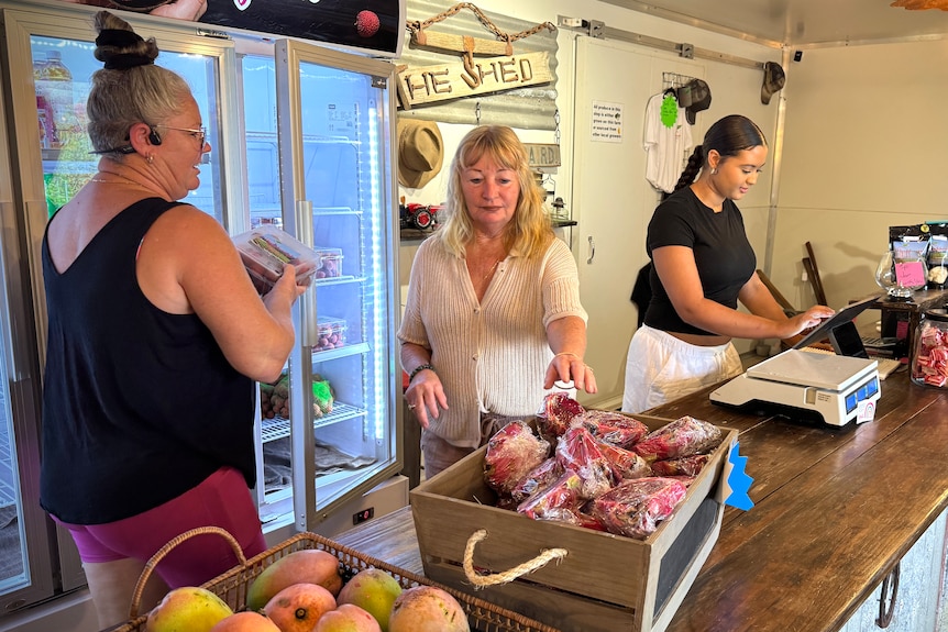 Three women organise fruit for customers in the shop.