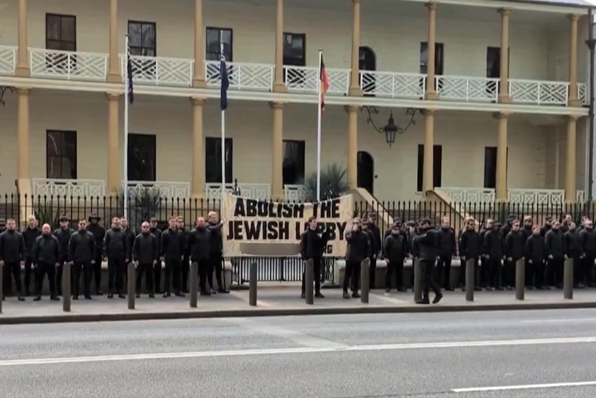 a groupd of about sixty people from the National Socialist Network dressed in black at a rally outside parliament house sydney