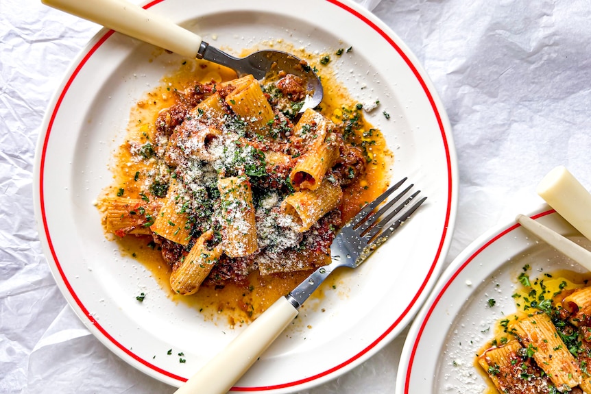 A plate of slow cooker bolognese served with rigatoni and sprinkled with Parmesan cheese and finely chopped parsley. A hands-