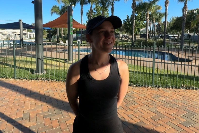 A woman wearing active wear and a cap in front of a pool.