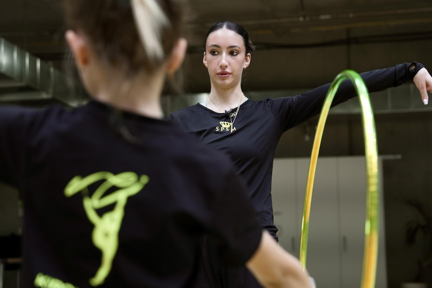 Retired rhythmic gymnast Alexandra Kiroi-Bogatyreva has her arm extended as she coaches a young girl holding a hoop