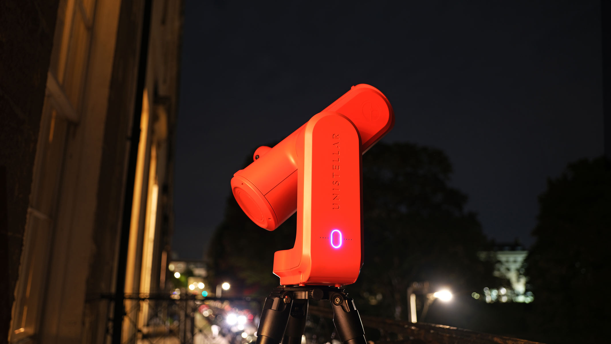 The Unistellar Odyssey Pro Red smart telescope pointing at the sky with bright streetlights and car headlights below it.