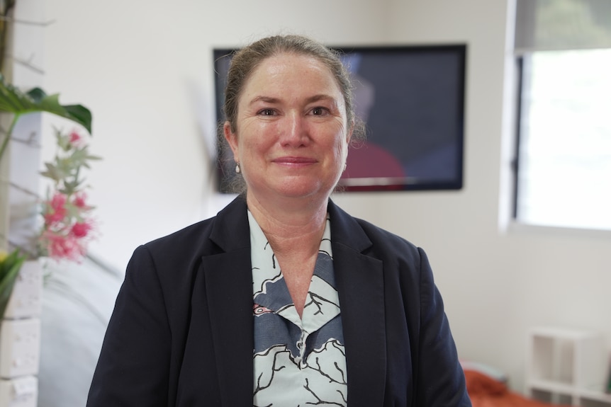 A woman with a blazer on in a school, smiling. 