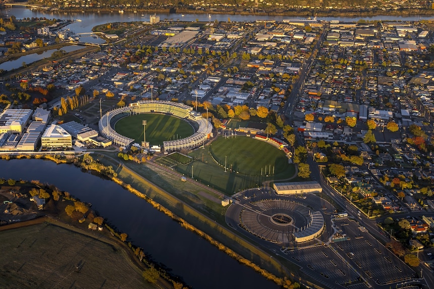 Aerial image of a sporting oval and city surrounds near a river.