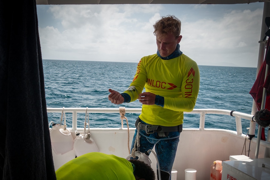 A man in a high-vis diving rash-vest on a boat on the ocean.
