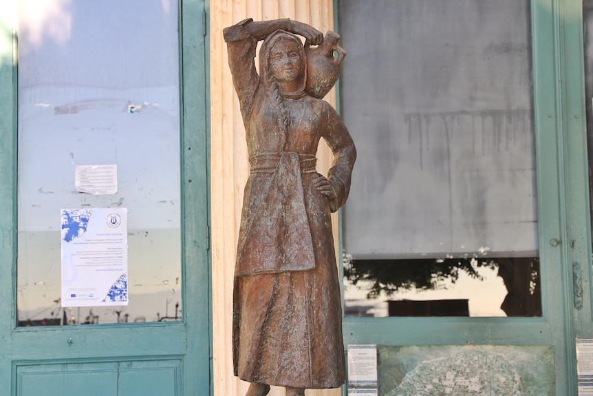 An image of a bronze statue of a woman, water bearer, holding a water vase over her head and hand on hip.