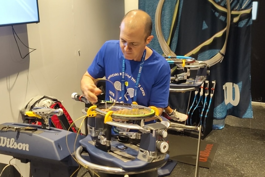 Man sits down stringing a tennis racquet