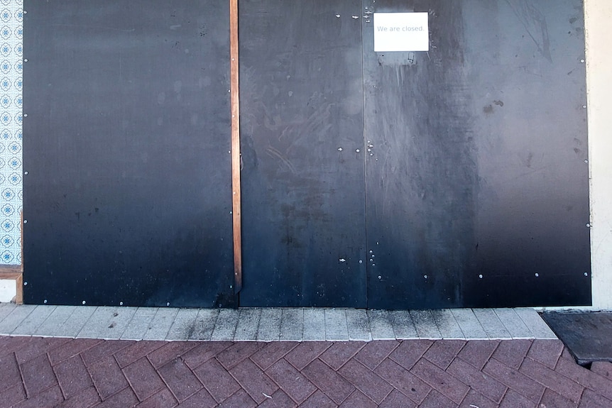 Burn marks on bricks, below a boarded up door. A sign says "closed".