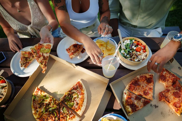 Three people filling their plates with pizza, salad and chips