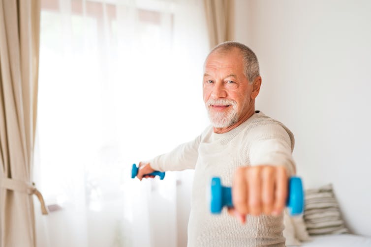 A man with grey hair using two small blue dumbbells