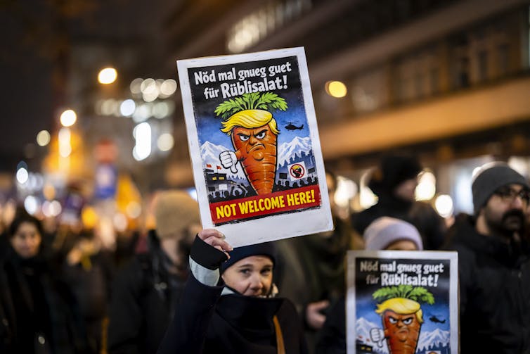 A protester holds a placard showing a caricature of US President Donald Trump and reading 'Not welcome to here!' during a rally against the World Economic Forum
