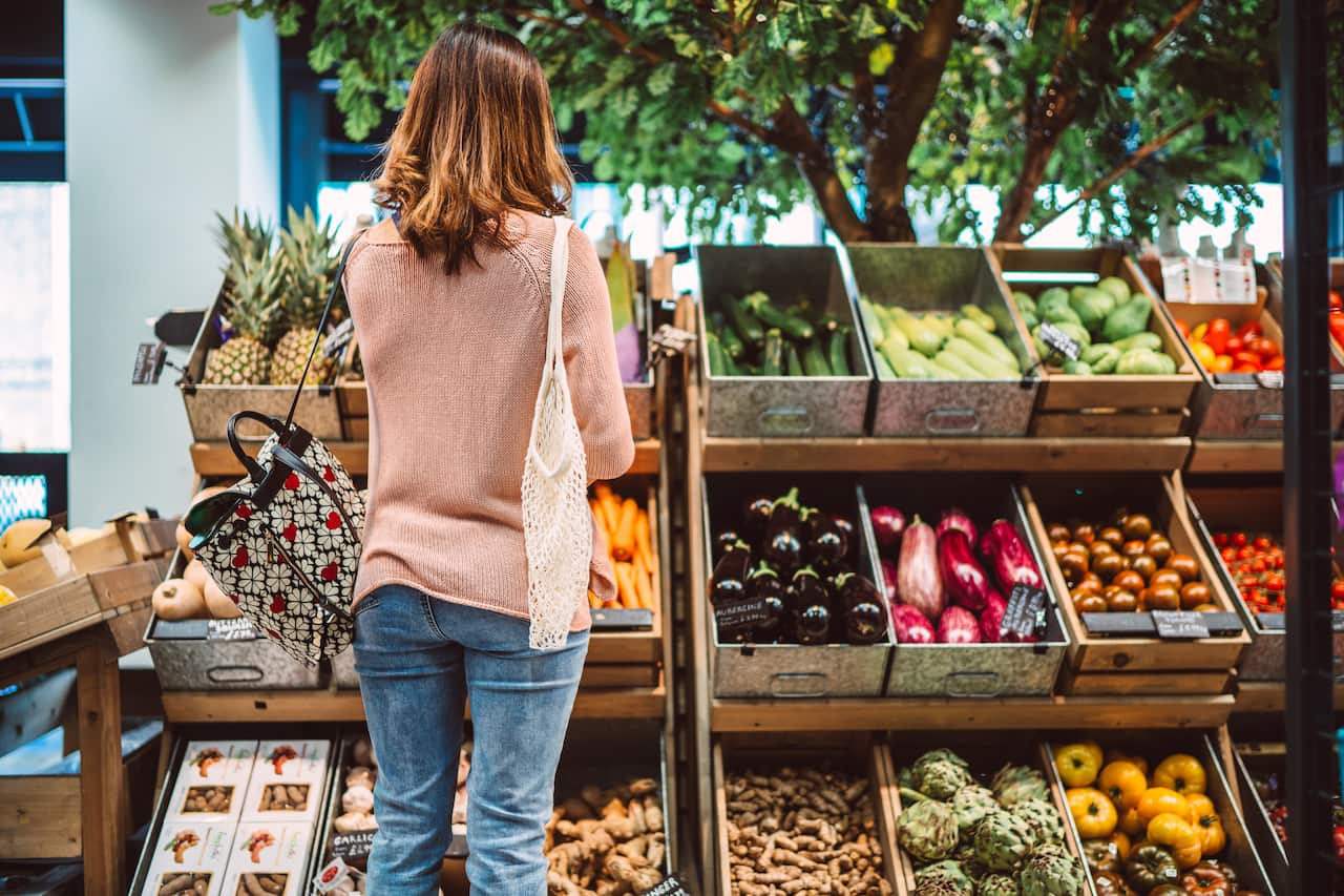 A woman stands in front of boxes of vegetables.