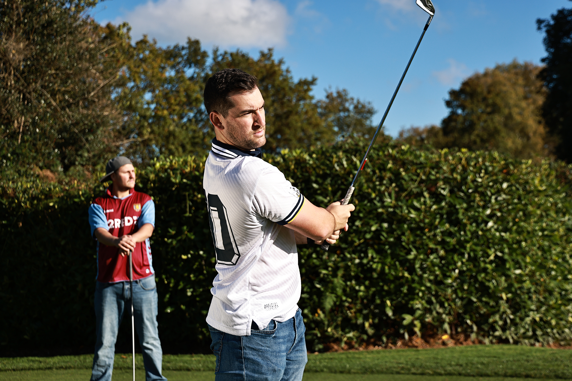 Sam De'ath in the finish position with an iron, wearing a football shirt, with Nick Bonfield in the background also wearing a football shirt and a backwards cap