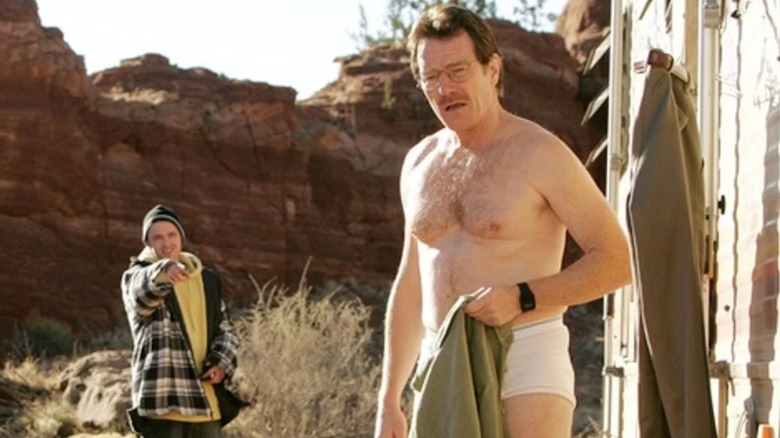 Walter White holding a green shirt while wearing white underpants as Jesse Pinkman stands behind him and points in 