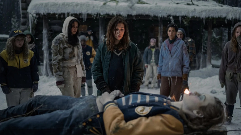Sophie Nélisse as Shauna Shipman standing in front of Jackie's frozen corpse as she is laid out on a table while the other girls stand behind her in shock in "Yellowjackets"