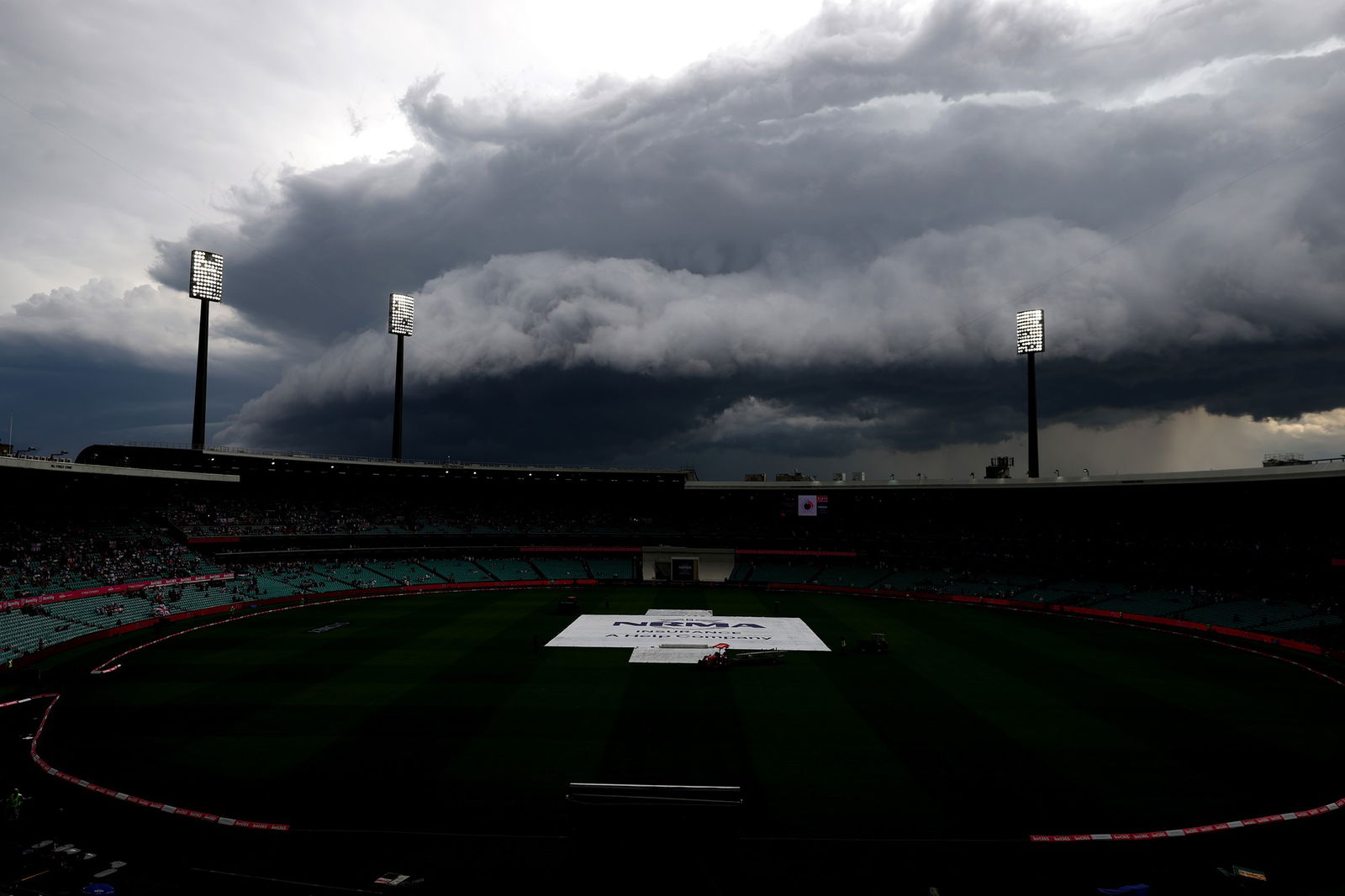 A landscape shot of a cricket ground with covers in place and large, dark clouds overhead.