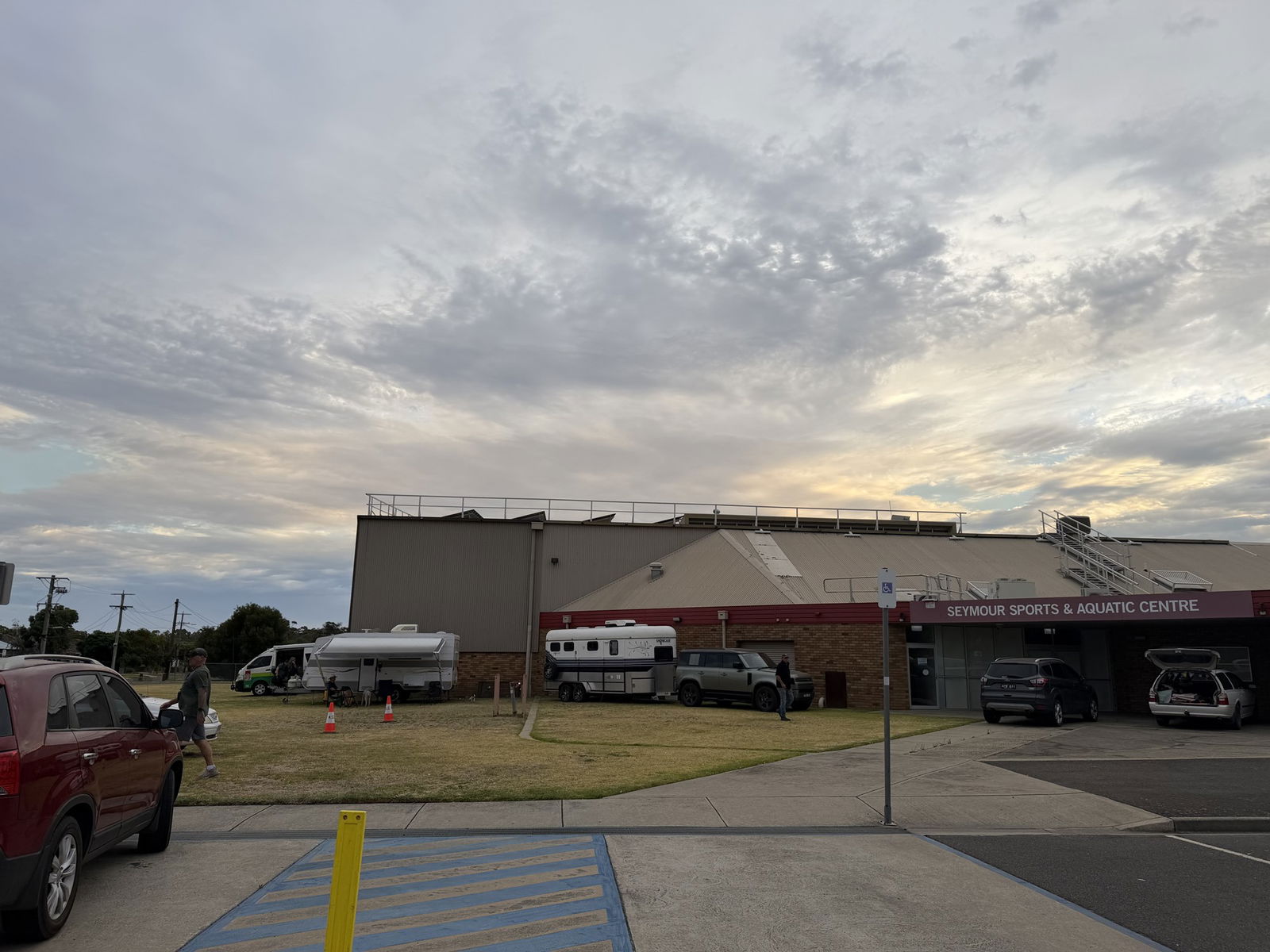 Cars are parked outside a beige brick building. A sign outside reads 'Seymour Sports 