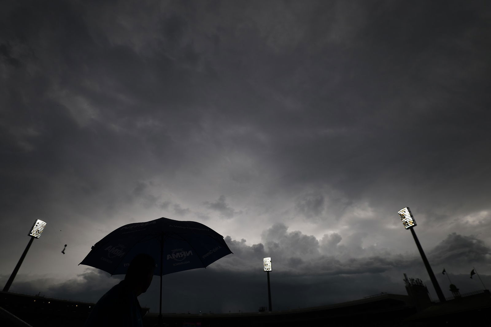 A landscape shot of a cricket ground with covers in place and large, dark clouds overhead.