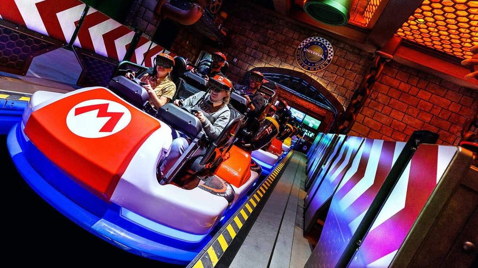 People in Mario-themed kart ride wearing VR headsets indoors at a theme park.