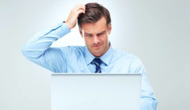 An ASX investor in a business shirt and tie looks at his computer screen and scratches his head.