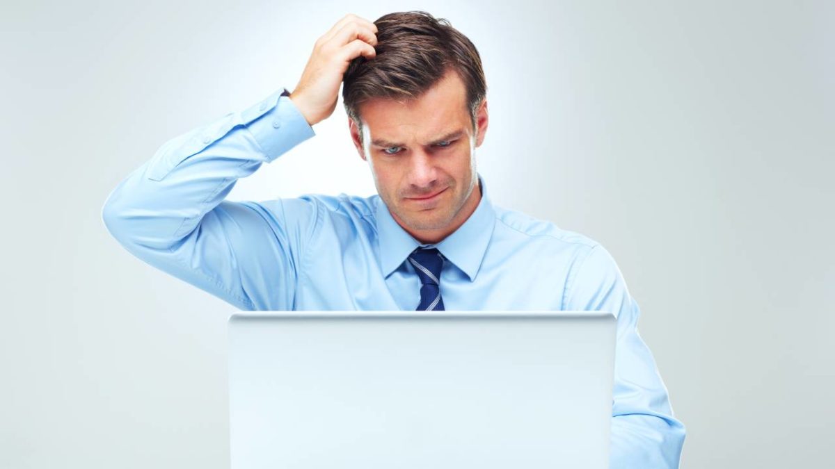 An ASX investor in a business shirt and tie looks at his computer screen and scratches his head.
