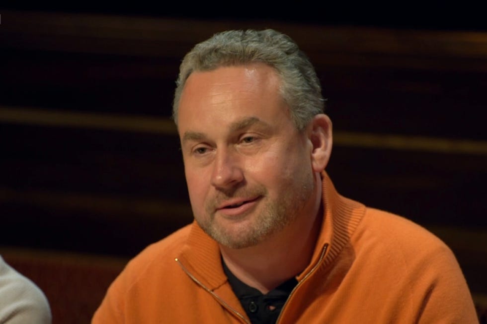man in an orange sweater engaged in a discussion