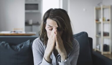 A woman is sitting on a couch with her hands on her face. She has a look of distress on her face.