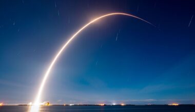 A time lapse photo captures the break streak of a rocket launching into the early morning dark blue sky over a body of water