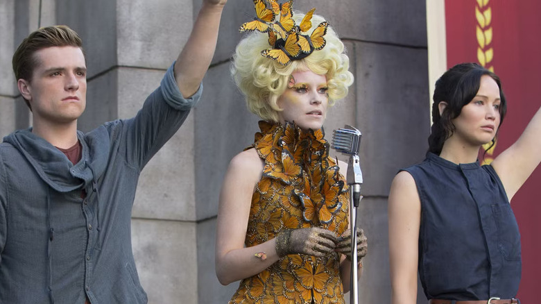 Peeta and Katniss saluting a District 11 crowd with a confused Effie Trinket in The Hunger Games: Catching Fire