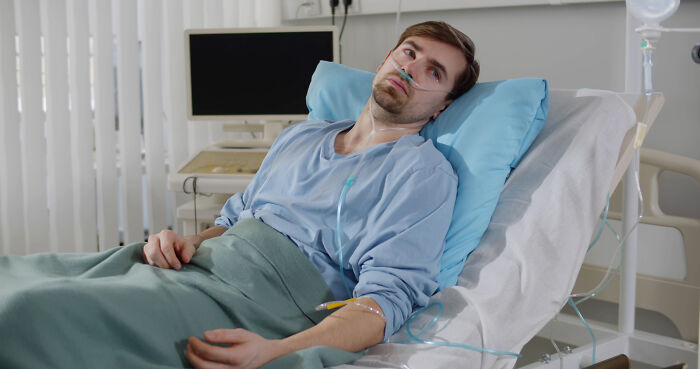 Young male patient in hospital bed with nasal oxygen, looking away while receiving medical care before leaving against advice.