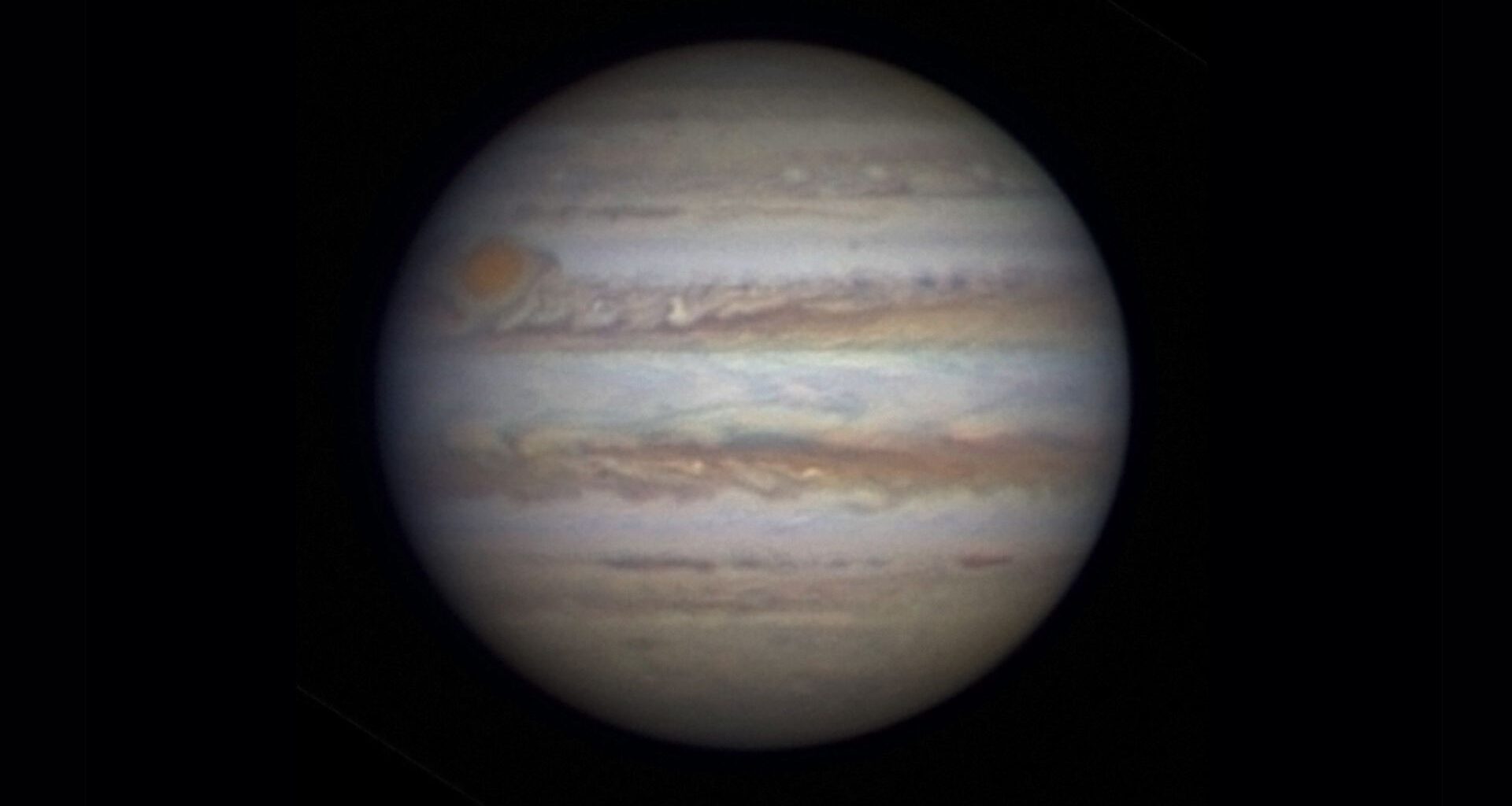 Photo of Jupiter as seen through a telescope. A large white sphere with swirling rings of red and brown around it against a black background.