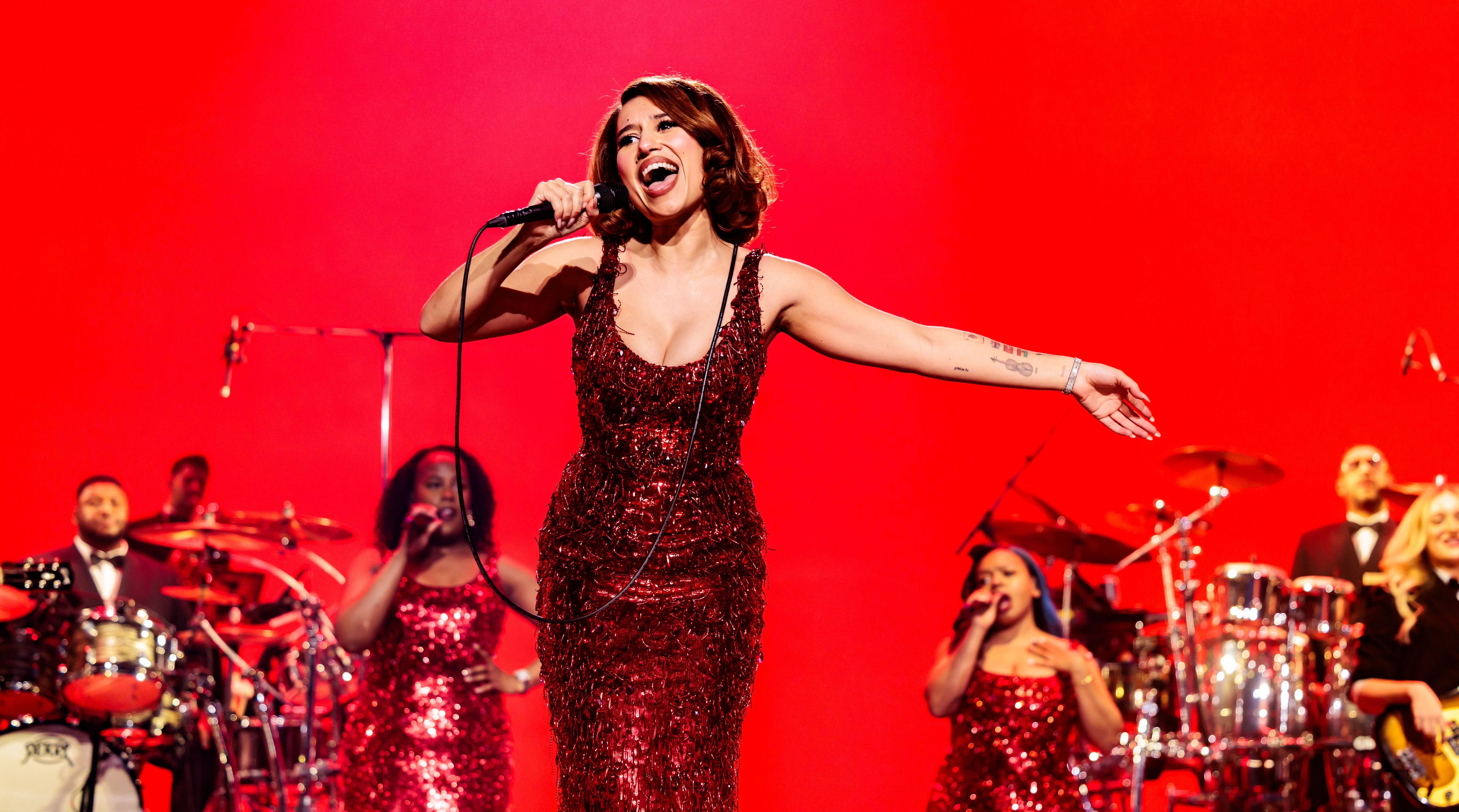 Singer Raye performing in a red sequined dress, holding a microphone.