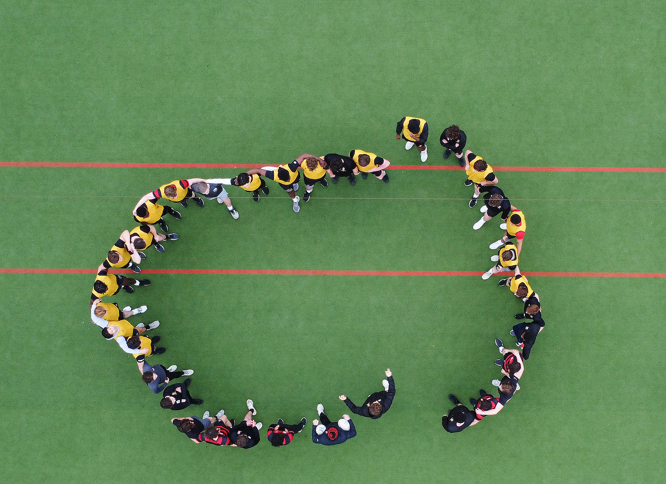 Aerial view of rugby players forming a large cup shape on a green field.