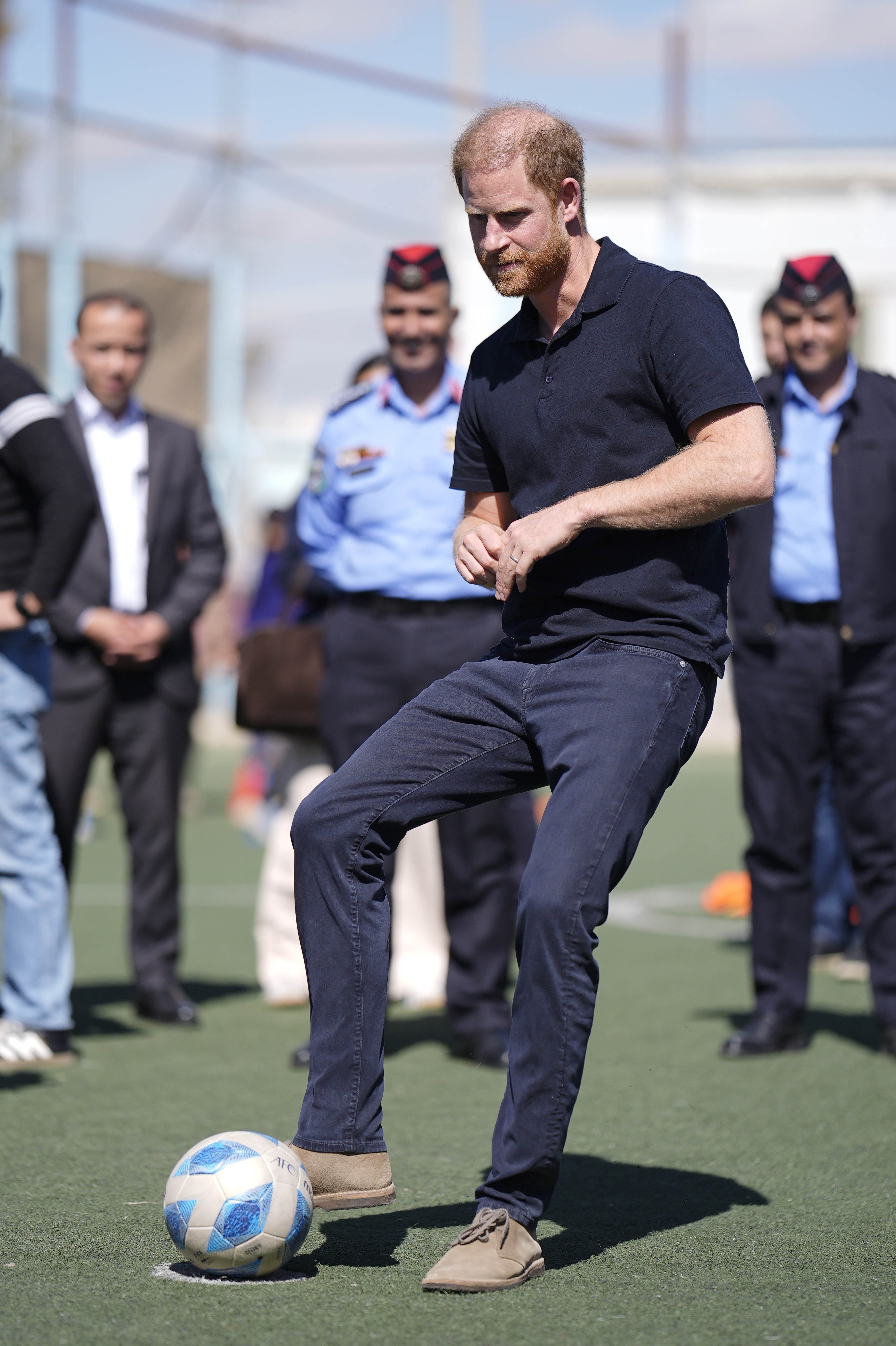 The Duke of Sussex takes a penalty shot on a green sports field.