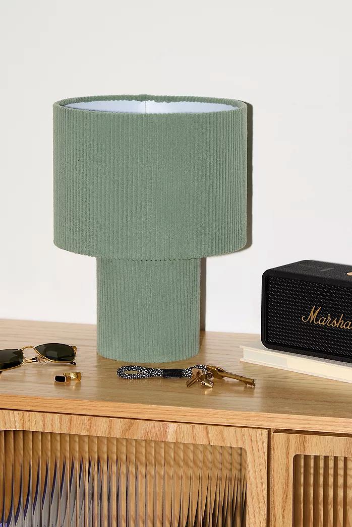 A Cord Urban Outfitters lamp with a green corduroy shade and base, sunglasses, keys, and a Marshall speaker on a wooden table.