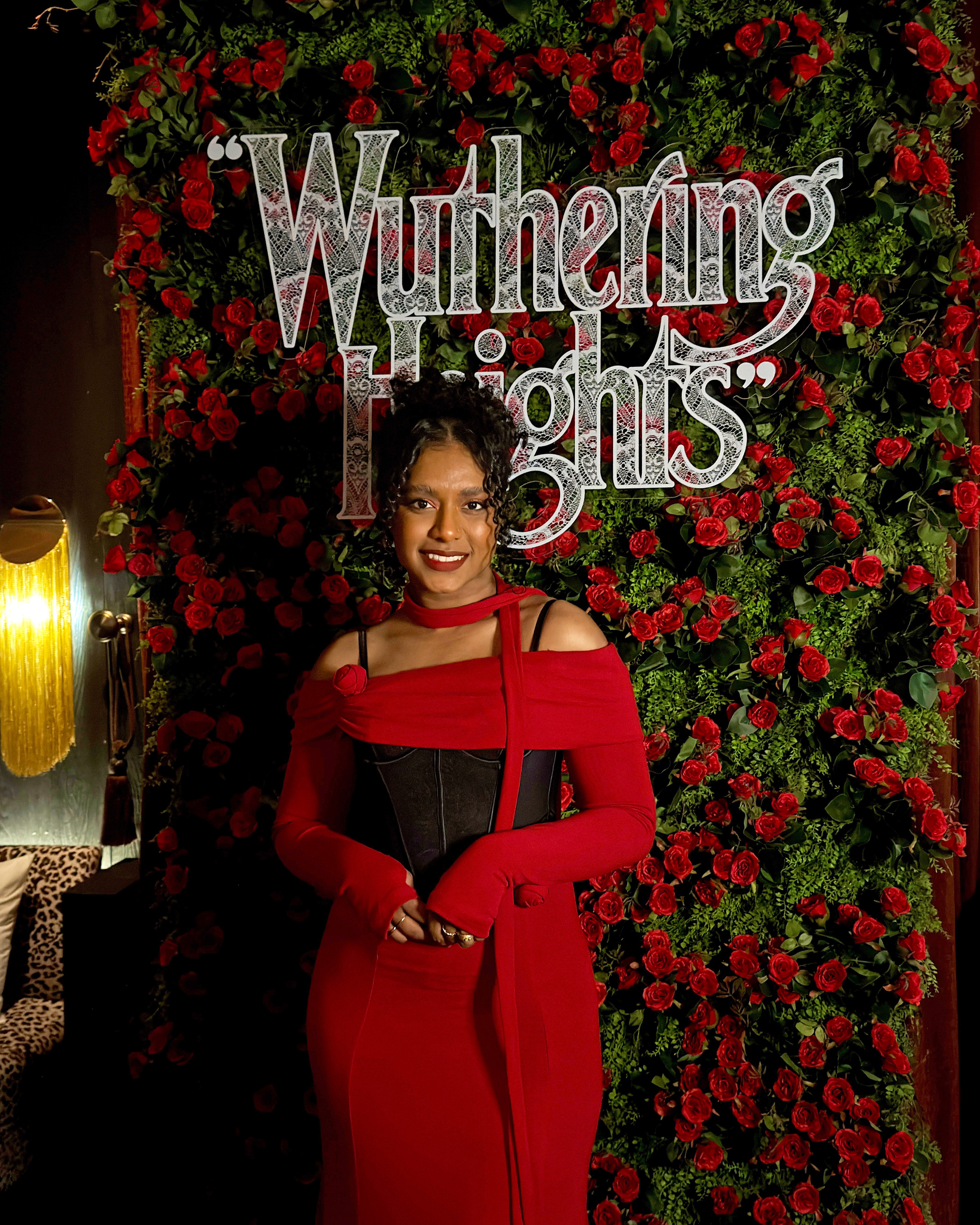 Jananie Velu standing in front of a red rose and green foliage background with the title "Wuthering Heights" in white lace-patterned letters.