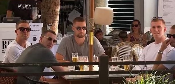 Several men wearing sunglasses seated at an outdoor restaurant table.
