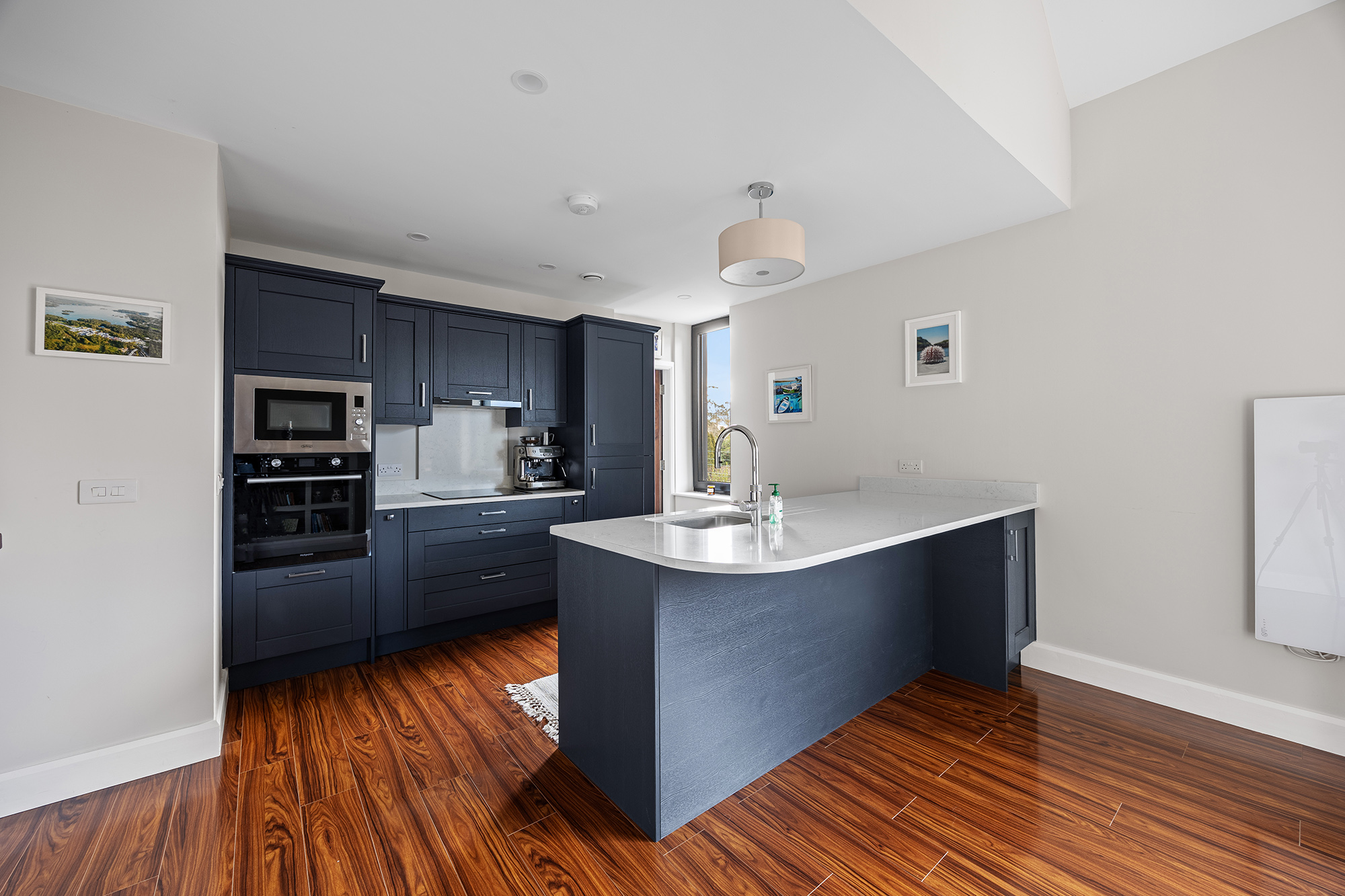 A kitchen with dark blue cabinets, hardwood floors, and a white marble counter island with a sink.