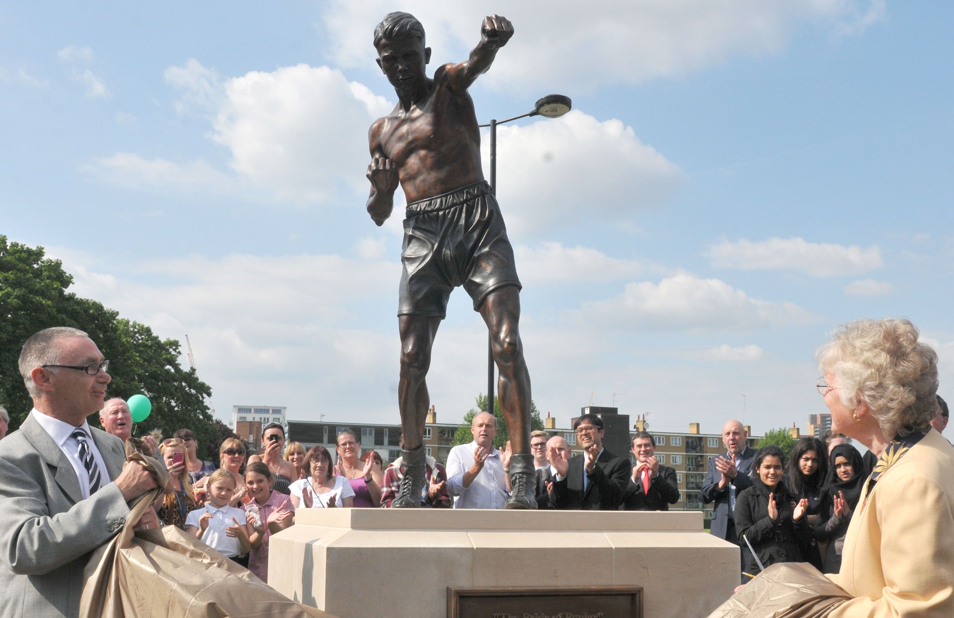 People unveiling a life-size statue of Teddy Baldock in a boxing pose.
