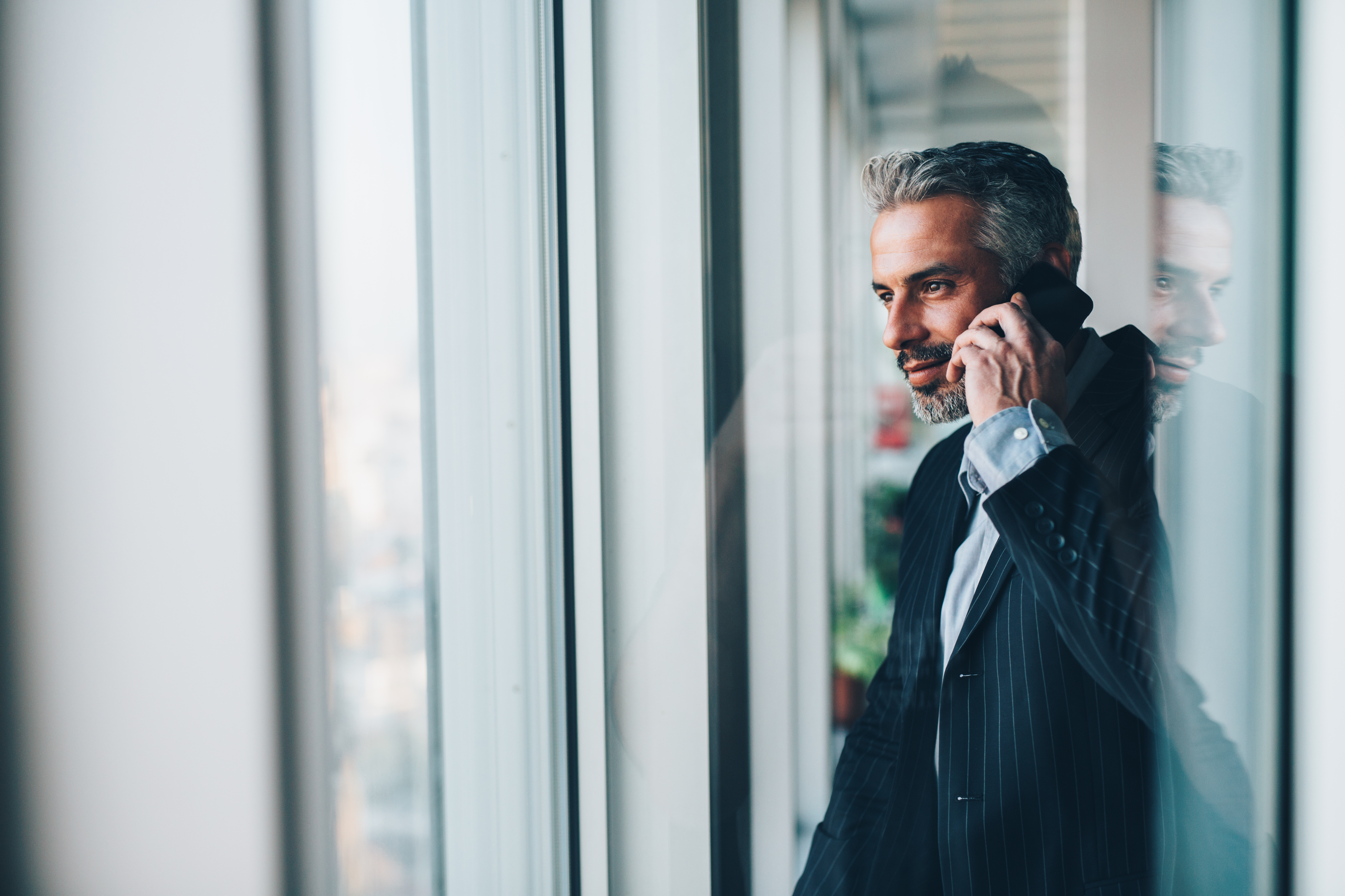 Mature businessman talking on the phone while looking out the window.