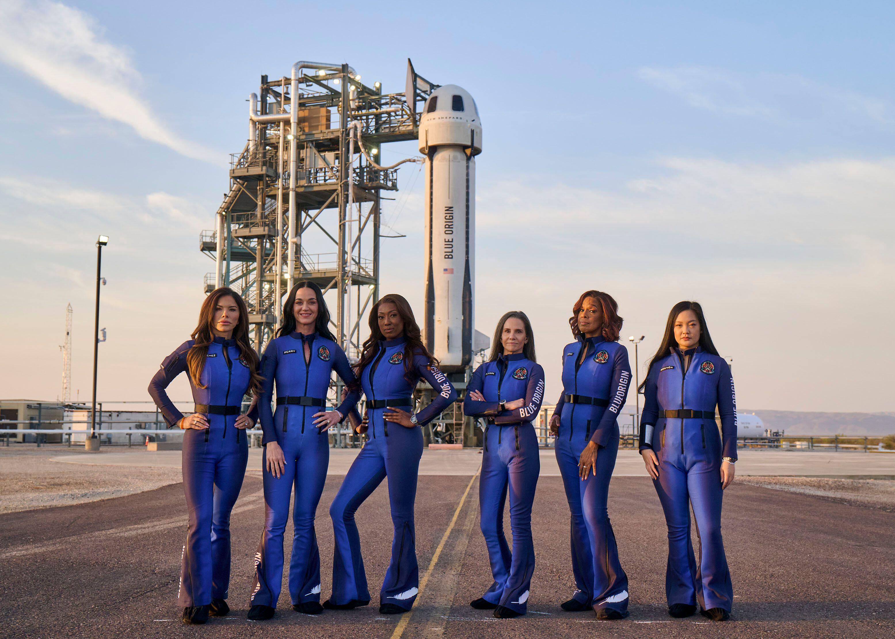 Lauren Sánchez, Katy Perry, Aisha Bowe, Kerianne Flynn, Gayle King, and Amanda Nguy?n in blue flight suits in front of a Blue Origin rocket.