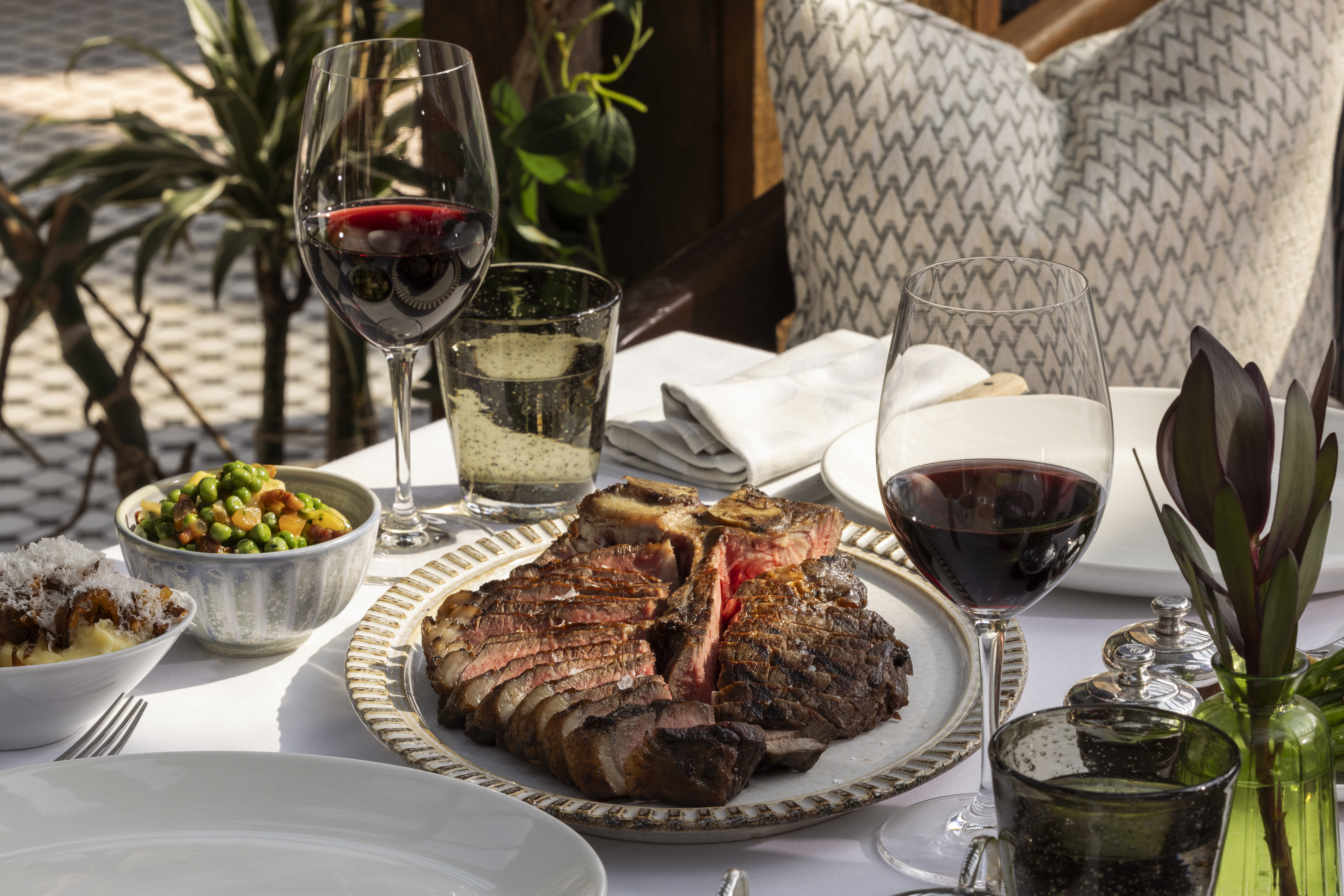 Sliced steak, mashed potatoes, and peas on a dining table with red wine.