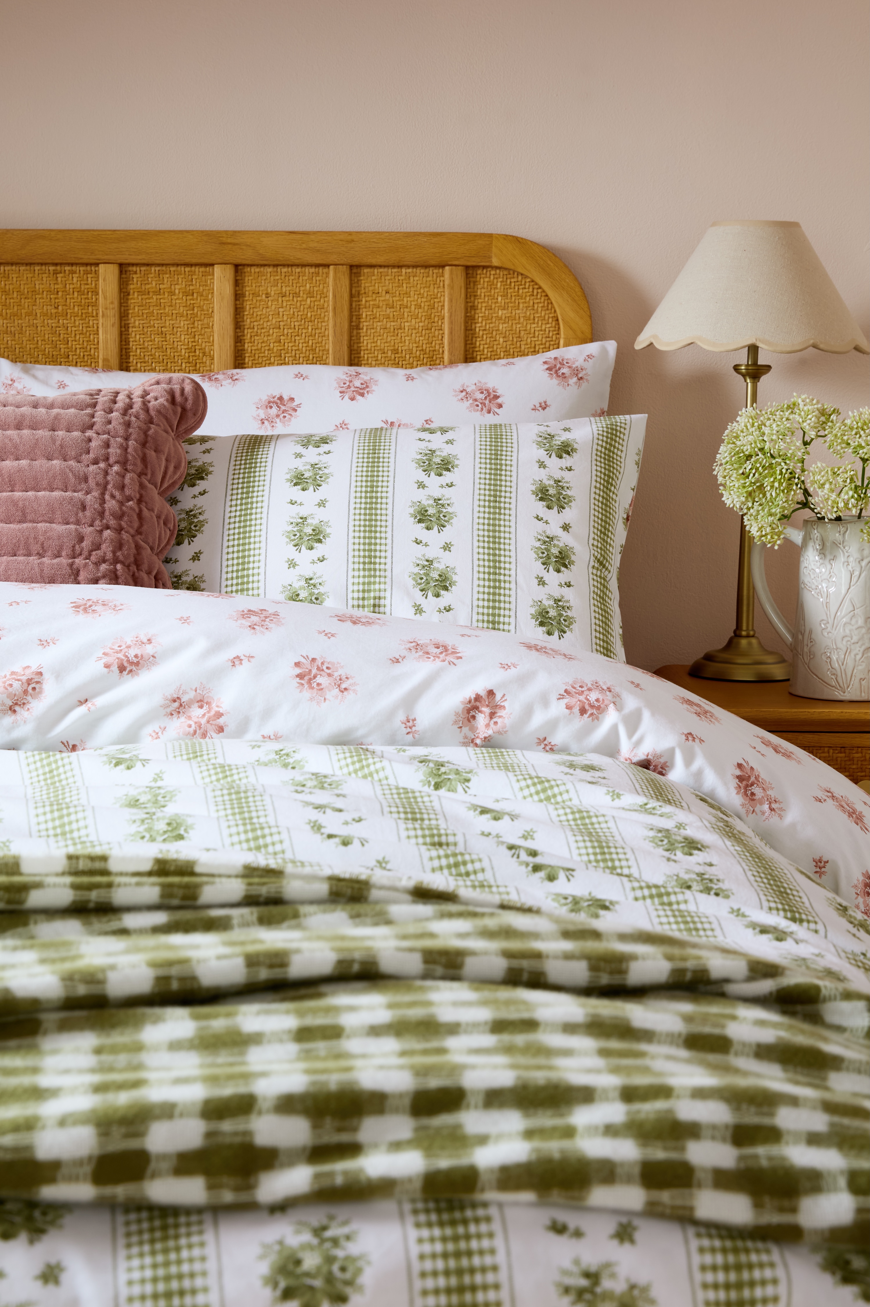 A bed with a wicker headboard and bedding in sage, pink, and white floral patterns.